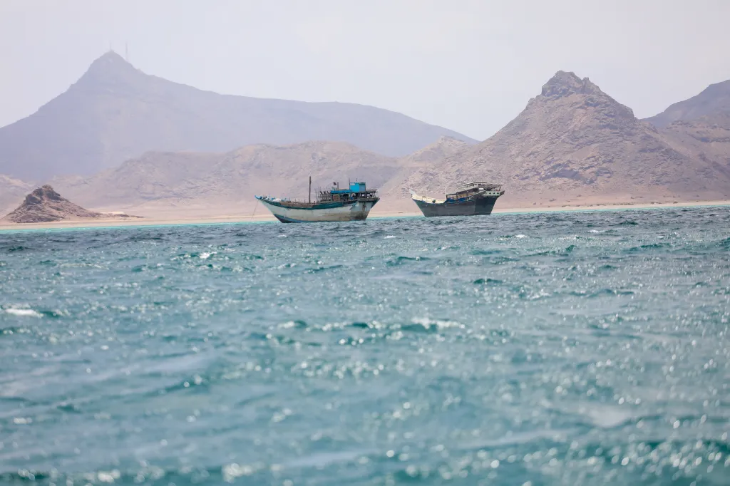 Two boats float in the Bab el-Mandeb strait off the coast of Yemen, with mountains in the background.