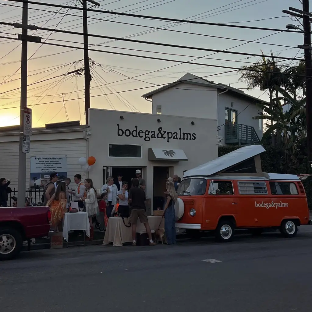 The Bodega & Palms storefront with an orange vintage van parked outside and people gathered for an event.