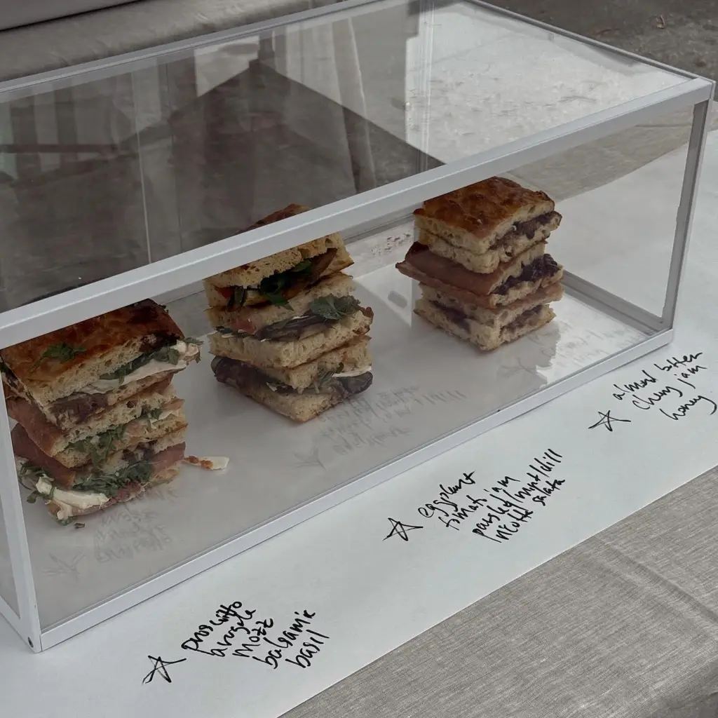 Three distinct focaccia sandwiches, each with handwritten labels indicating ingredients like "prosciutto," "eggplant," and "almond butter."