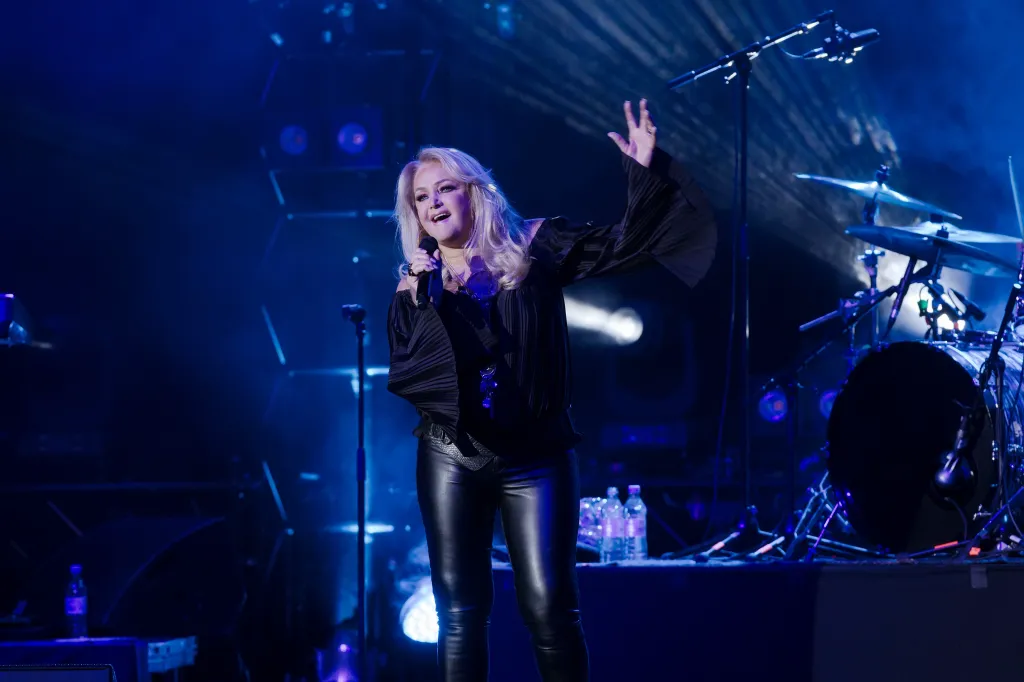 Bonnie Tyler performing on stage with a microphone in her hand, dressed in black.