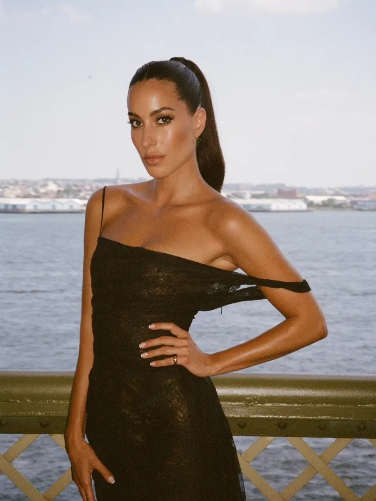 Ines de Ramon in a black sheer off-the-shoulder dress by the water.