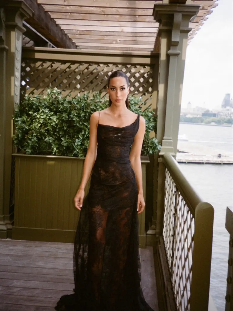 Ines de Ramon in a black lace dress on a balcony overlooking water.