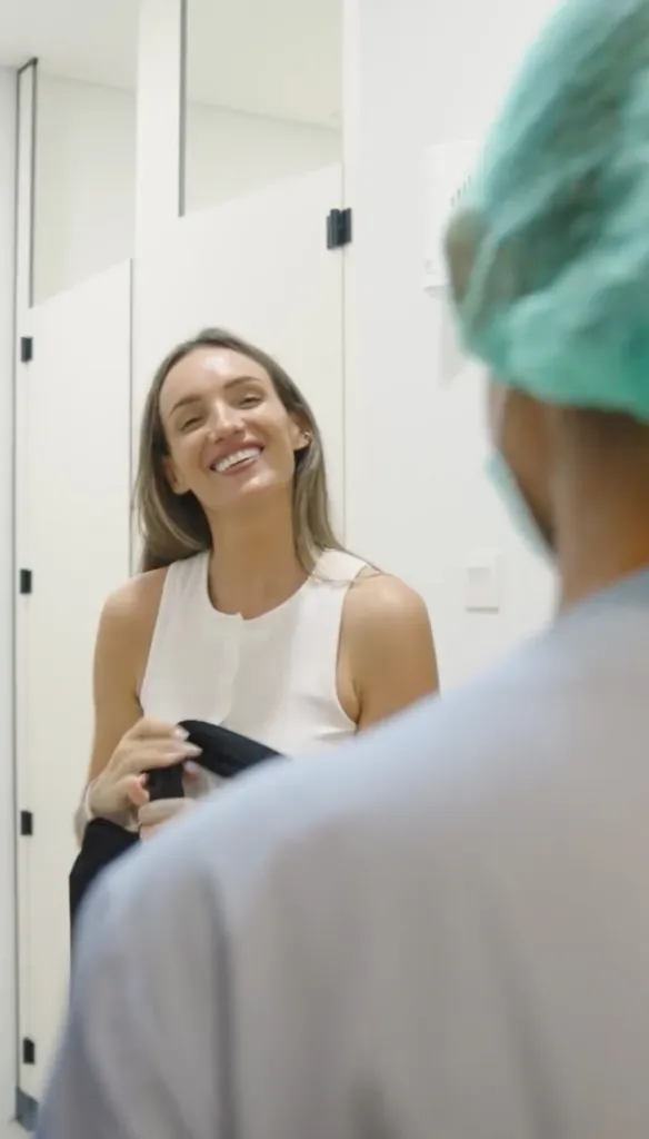 A woman in a white top smiles at someone in medical scrubs and cap.