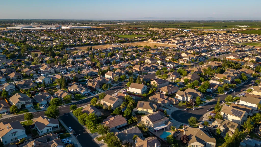 Aerial view of a Manteca, California suburban neighborhood with houses, streets, trees, and distant farmlands.