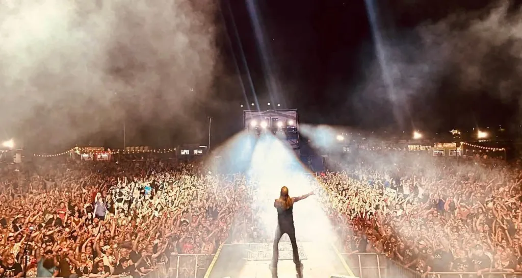 Bret Michaels performing on stage to a large crowd under bright spotlights.