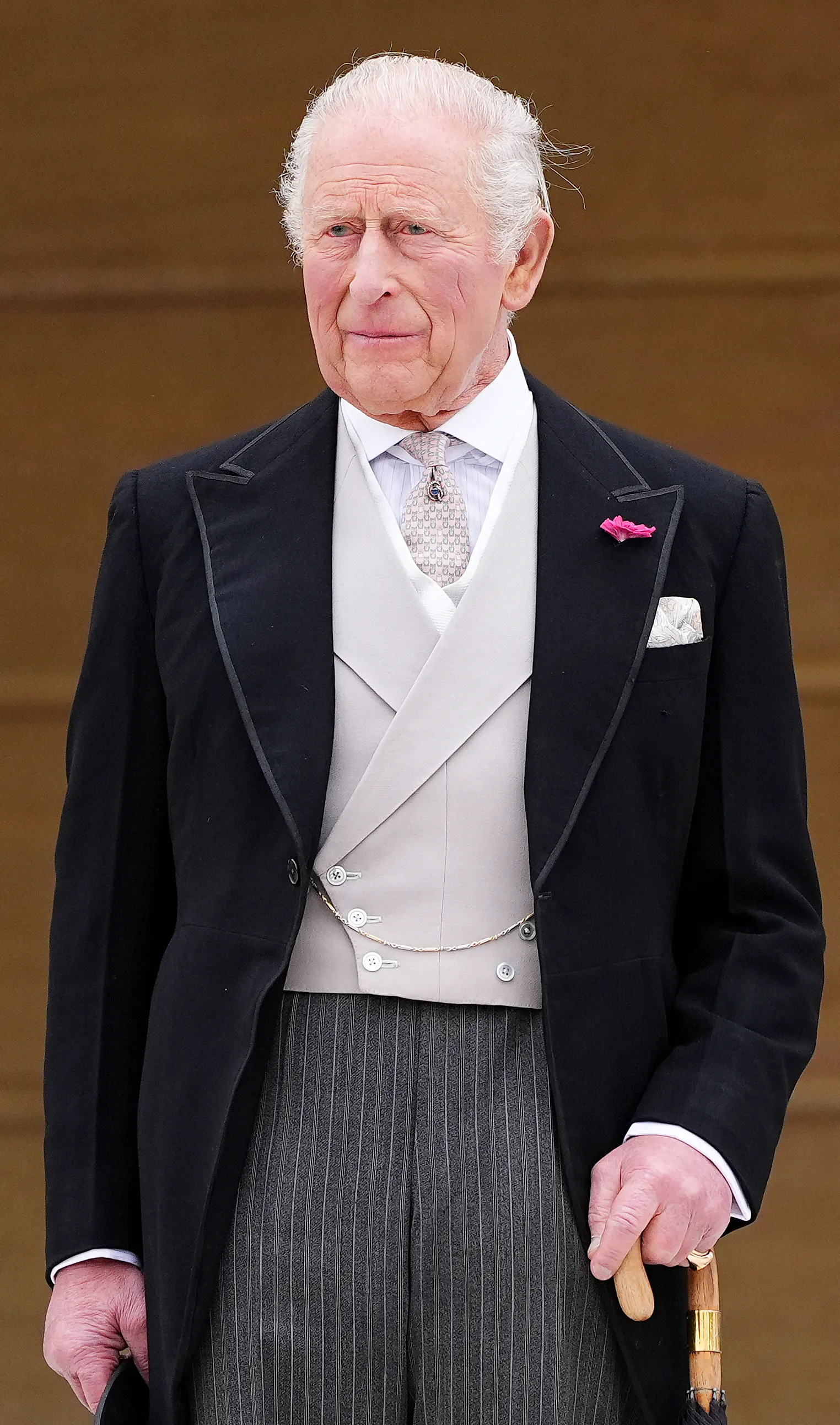 King Charles III in a morning coat, holding a walking stick.