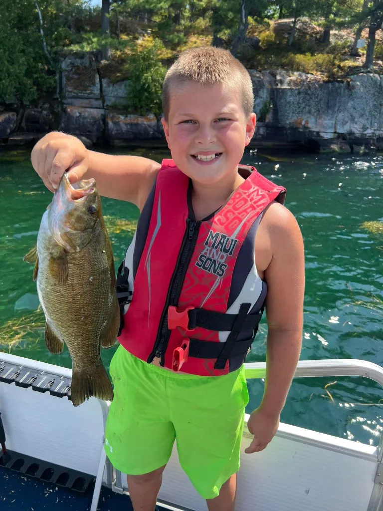 A boy in a life jacket holds up a fish he caught.