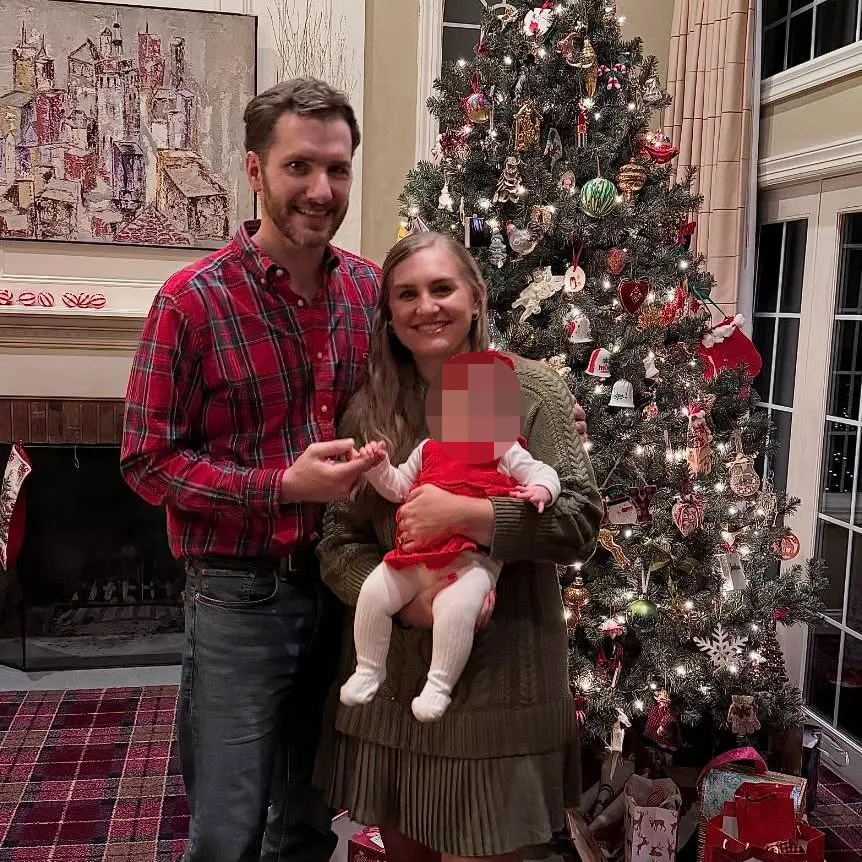 Brooke Hanlon with her husband and baby in front of a Christmas tree.