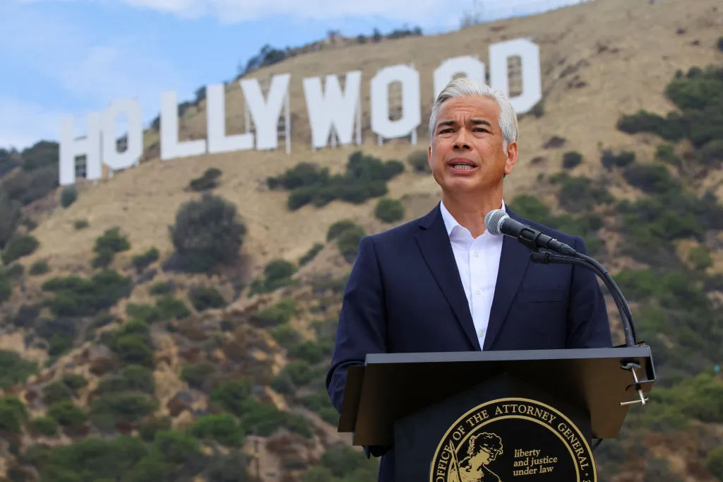 California Attorney General Rob Bonta speaks at a podium with the Hollywood sign visible in the background.