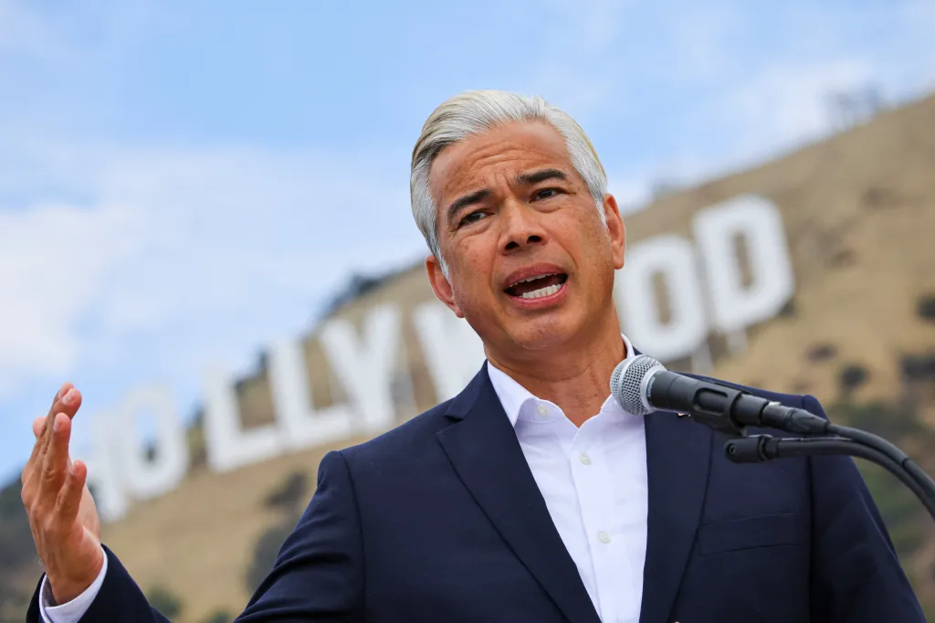 California Attorney General Rob Bonta speaking into a microphone with the Hollywood sign in the background.