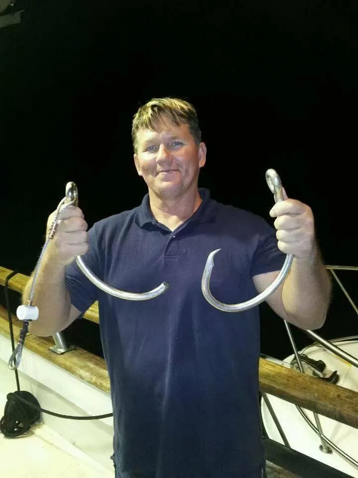 A man holds up two large, bent fishing hooks.