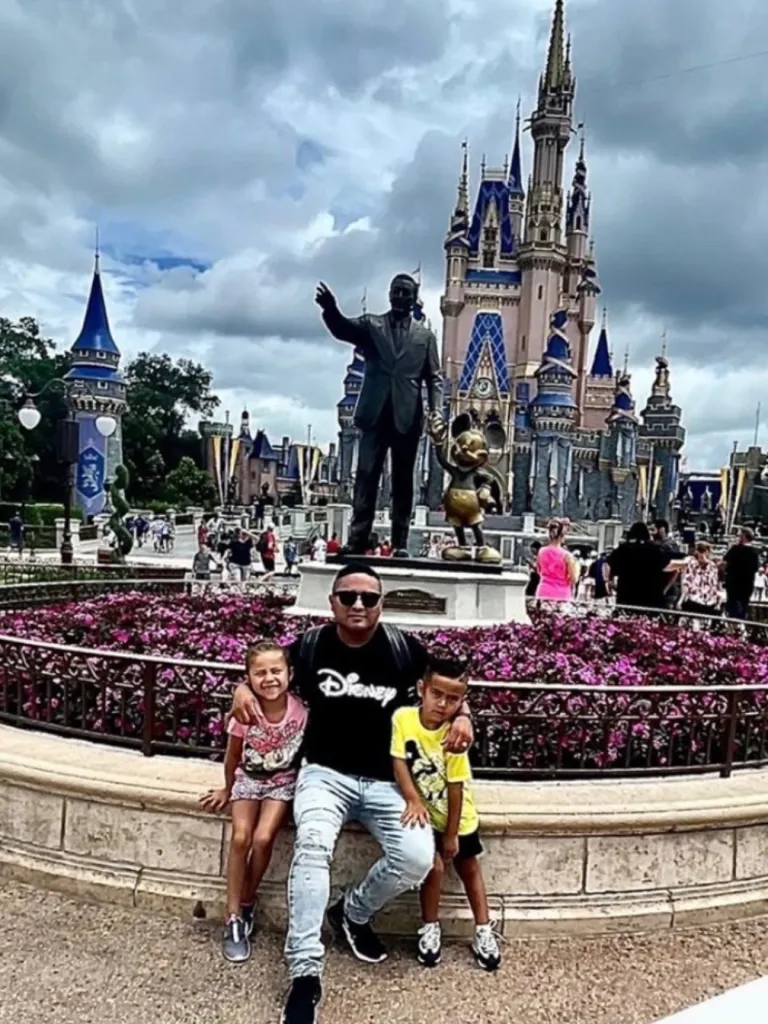 A man and two children pose in front of Cinderella Castle at Disney World.