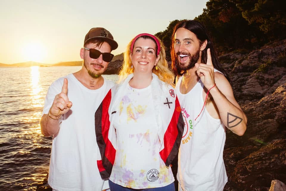 Two men and a woman posing for a photo with a sunset over the water in the background.
