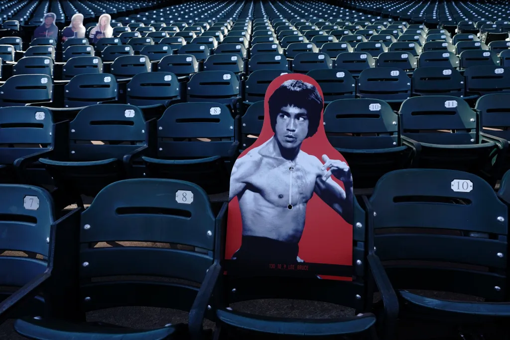 A cardboard cutout of martial artist Bruce Lee in a fighting pose, standing in an empty baseball stadium seat.