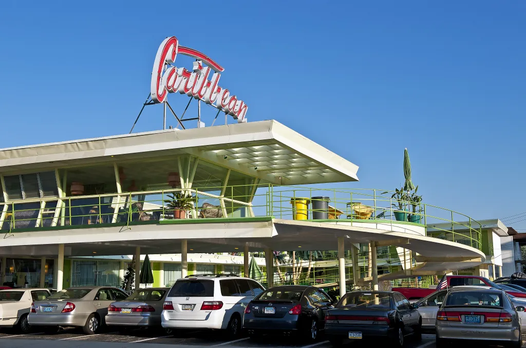 A retro 1950s Caribbean Motel in Wildwood, New Jersey, featuring a large neon sign, a second-story open-air lounge, and a parking lot full of cars.