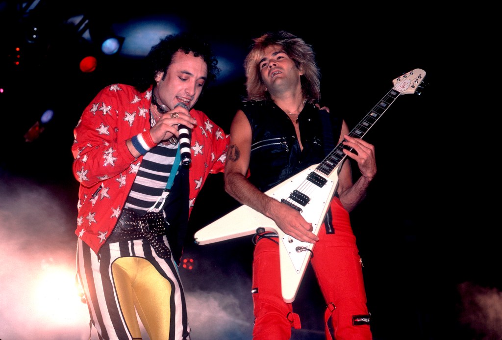 Kevin DuBrow singing into a microphone and Carlos Cavazo playing guitar on stage.