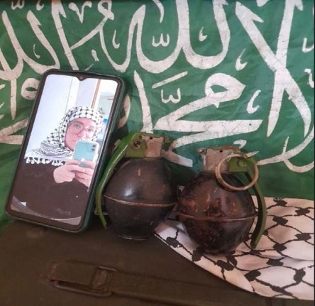 Catherine Washburn pictured with two hand grenades in front of Hamas flag.