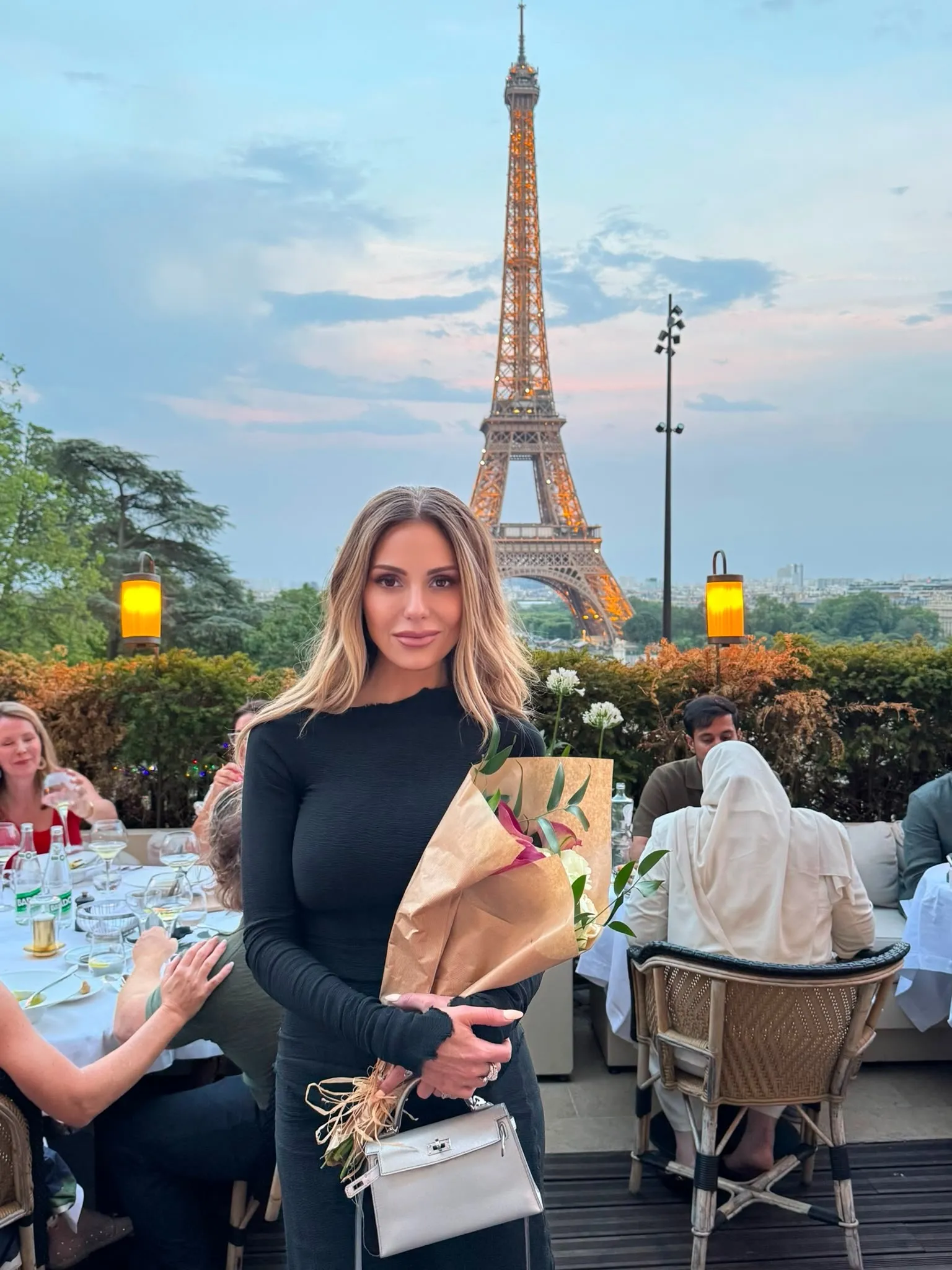 Dorit Kemsley holding flowers in front of the Eiffel Tower at an outdoor dinner party.