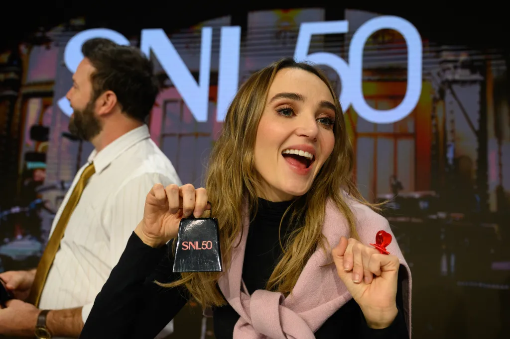 Chloe Fineman holding an "SNL50" cowbell and wearing a heart-shaped ring pop.