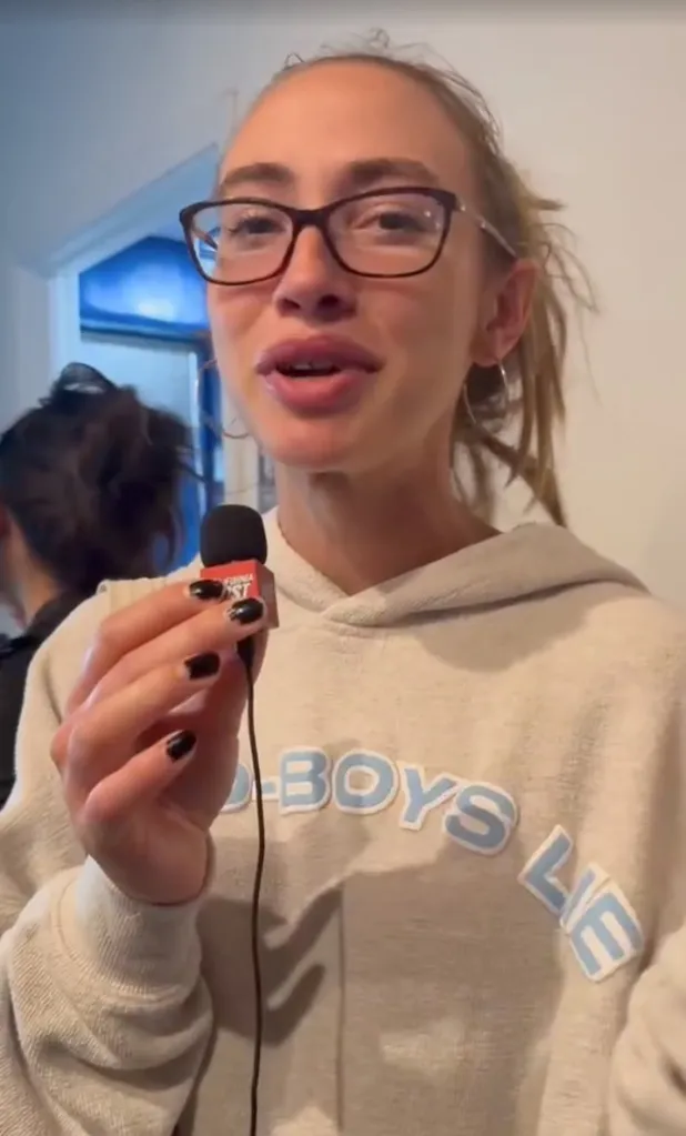 Claire Belhamer wearing glasses and a sweatshirt, holding a microphone.