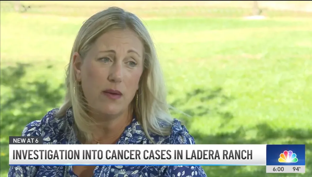 A blonde woman in a blue patterned shirt is interviewed outdoors, with text overlay "Investigation into cancer cases in Ladera Ranch."