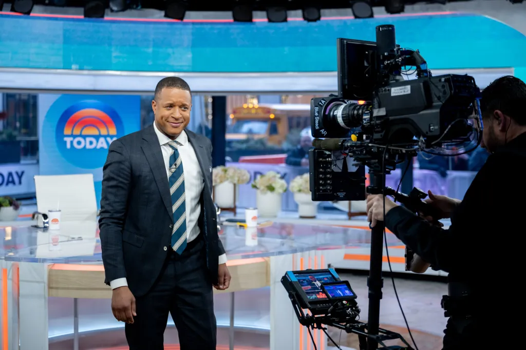 Craig Melvin on the set of the Today Show being filmed by a camera operator.