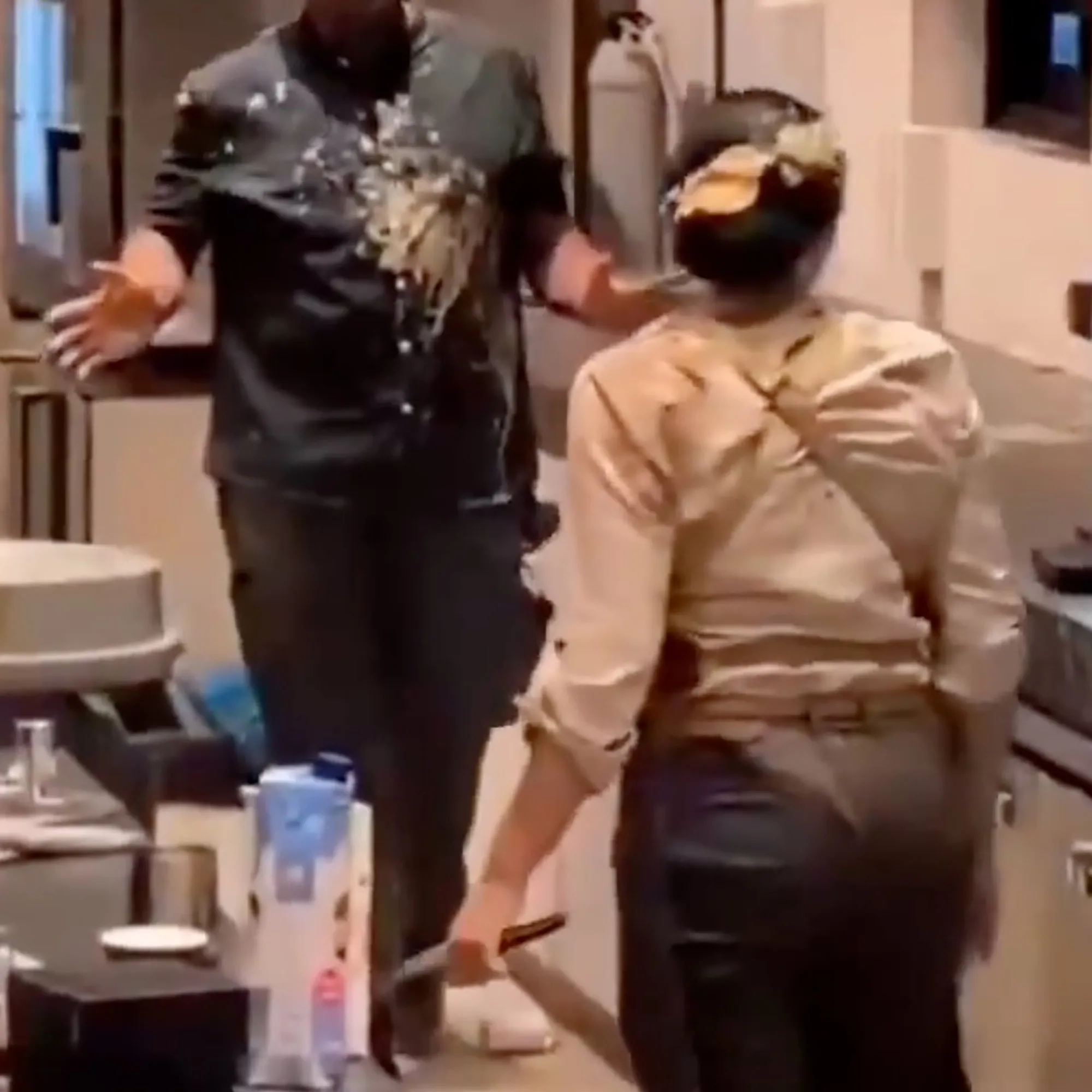 Two employees, one with food splattered on them, stand in a kitchen or serving area.