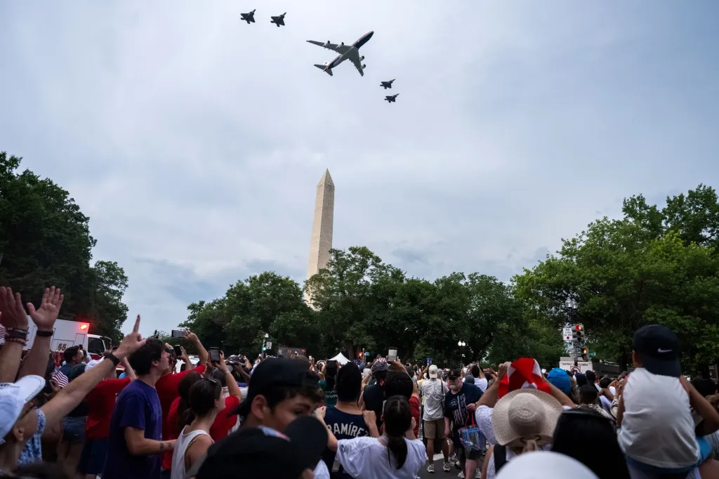 A large crowd gathers to watch a B-747 and four F-35 fighter jets fly over the Washington Monument.