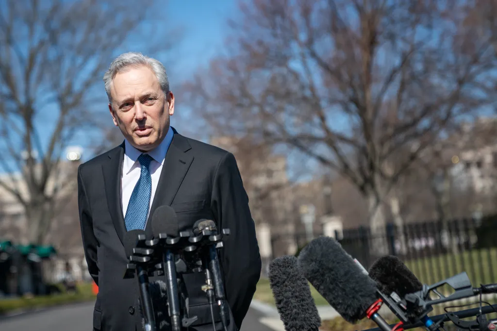 David Sacks, in a dark suit and blue tie, speaks into an array of microphones outside the White House.