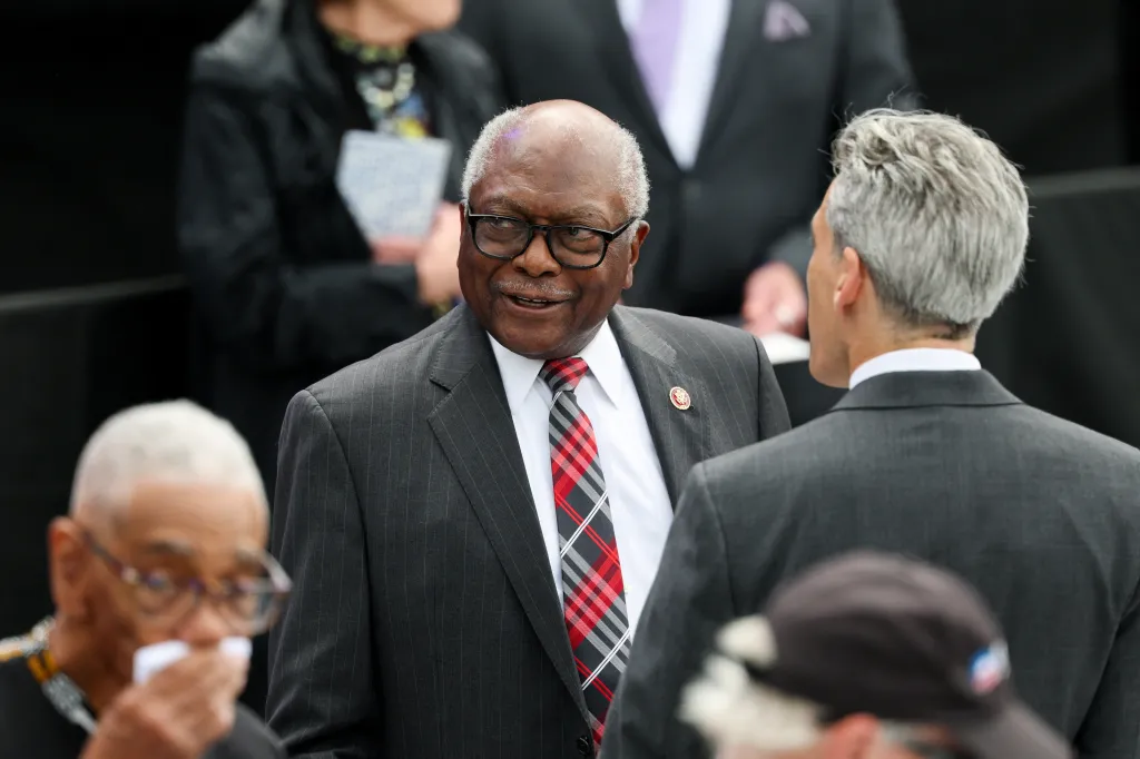 U.S. Representative James Clyburn in a pinstriped suit and plaid tie smiling at a man with gray hair.