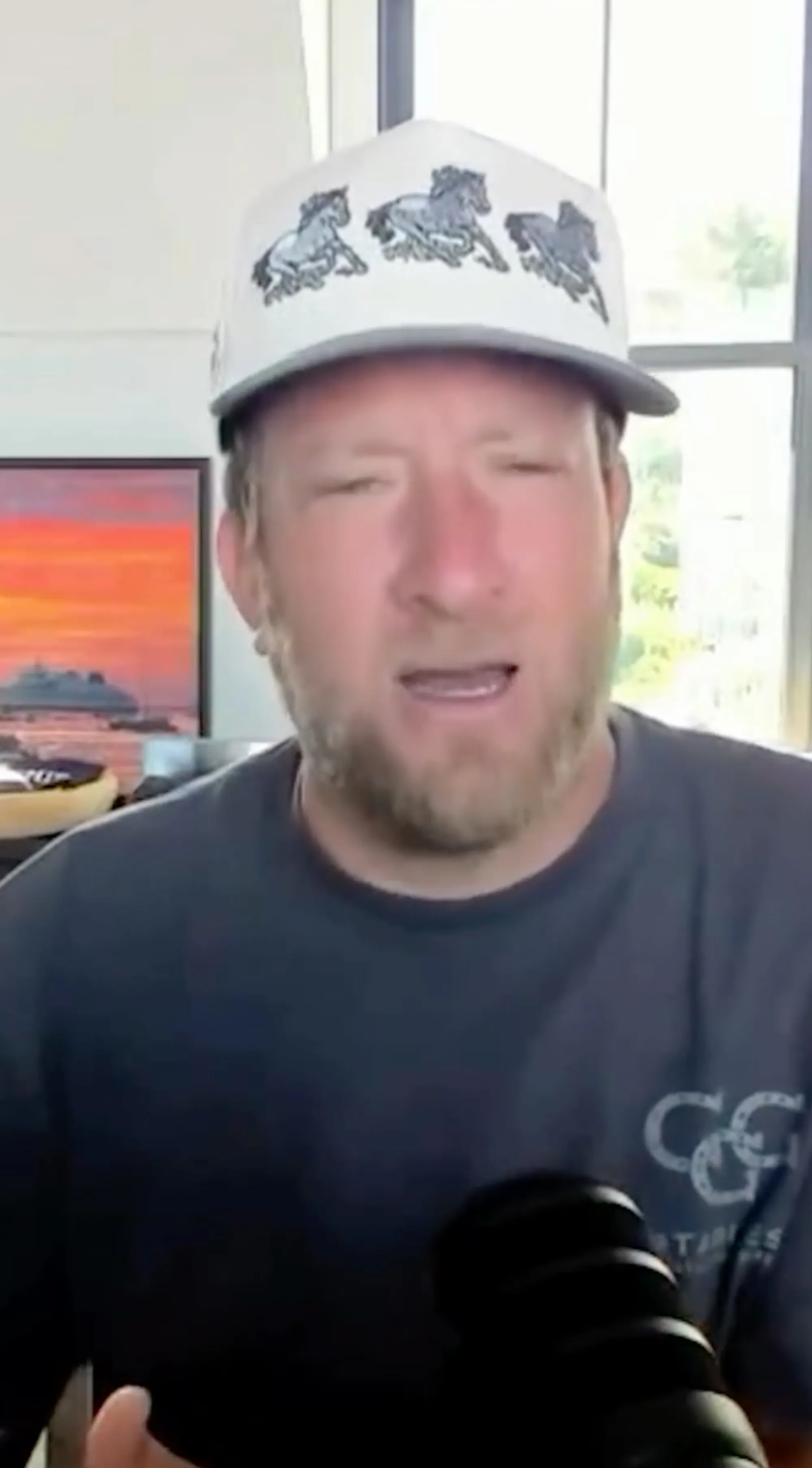 Dave Portnoy in a white hat with three horse graphics, speaking into a microphone.