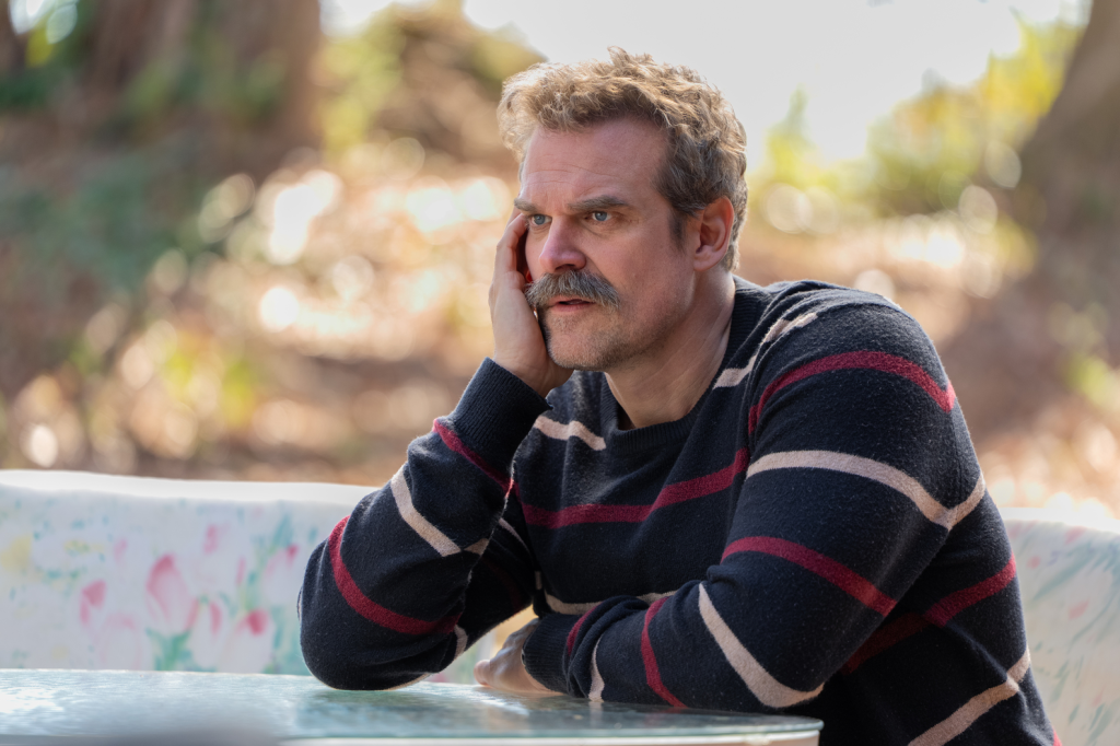 David Harbour in a striped sweater with his hand on his face.