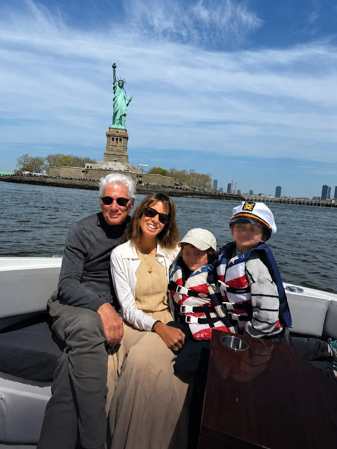 Richard Gere, his wife, and two children on a boat in front of the Statue of Liberty.