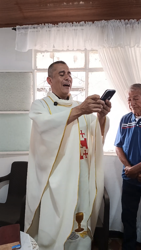 Gregorio Díaz Mora, wearing priestly vestments, holding a phone during Christmas Mass.