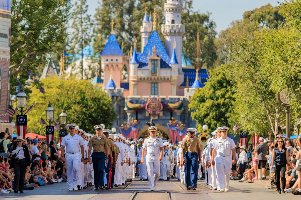 Military members march in a parade towards Disneyland's Sleeping Beauty Castle.