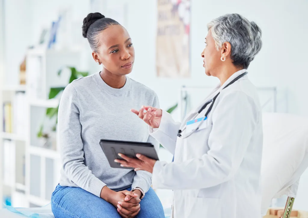 A doctor holding a tablet, talking to a patient.