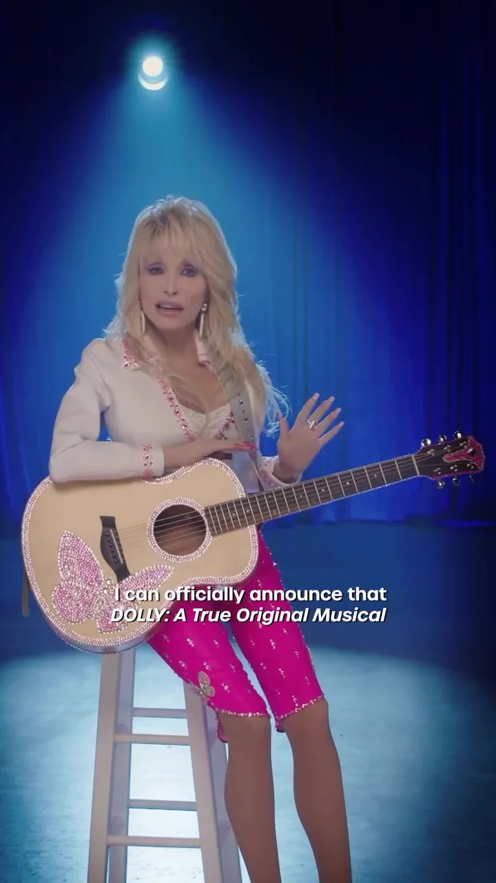 Dolly Parton in a white jacket and pink pants, seated on a stool and holding a rhinestone-studded guitar, with text announcing "DOLLY: A True Original Musical."