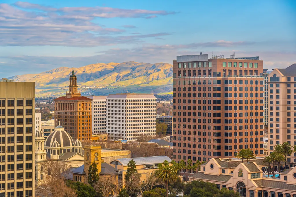 Downtown San Jose cityscape in Silicon Valley, California, at dusk, with buildings and mountains in the background.