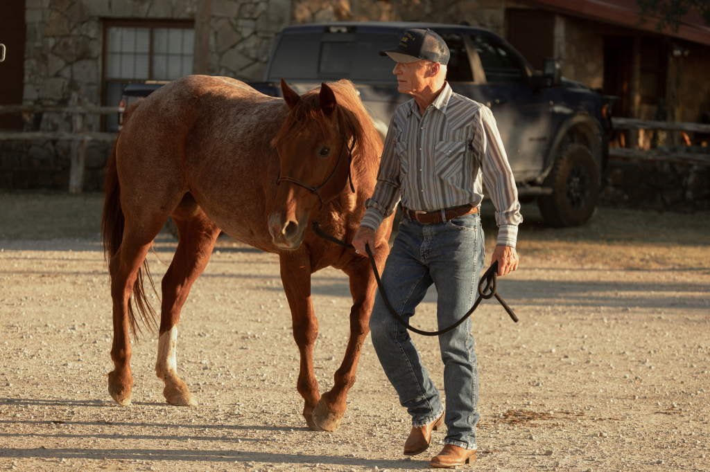 Ed Harris as Everett McKinney leading a brown horse on a dirt path.