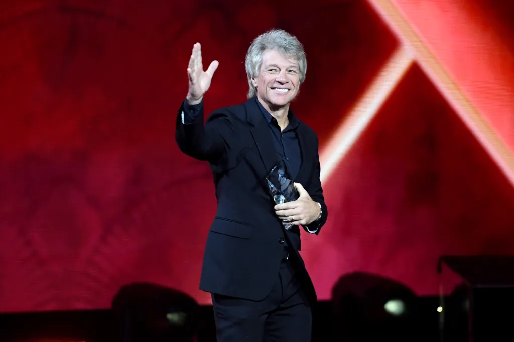 Jon Bon Jovi smiling and waving while holding an award.