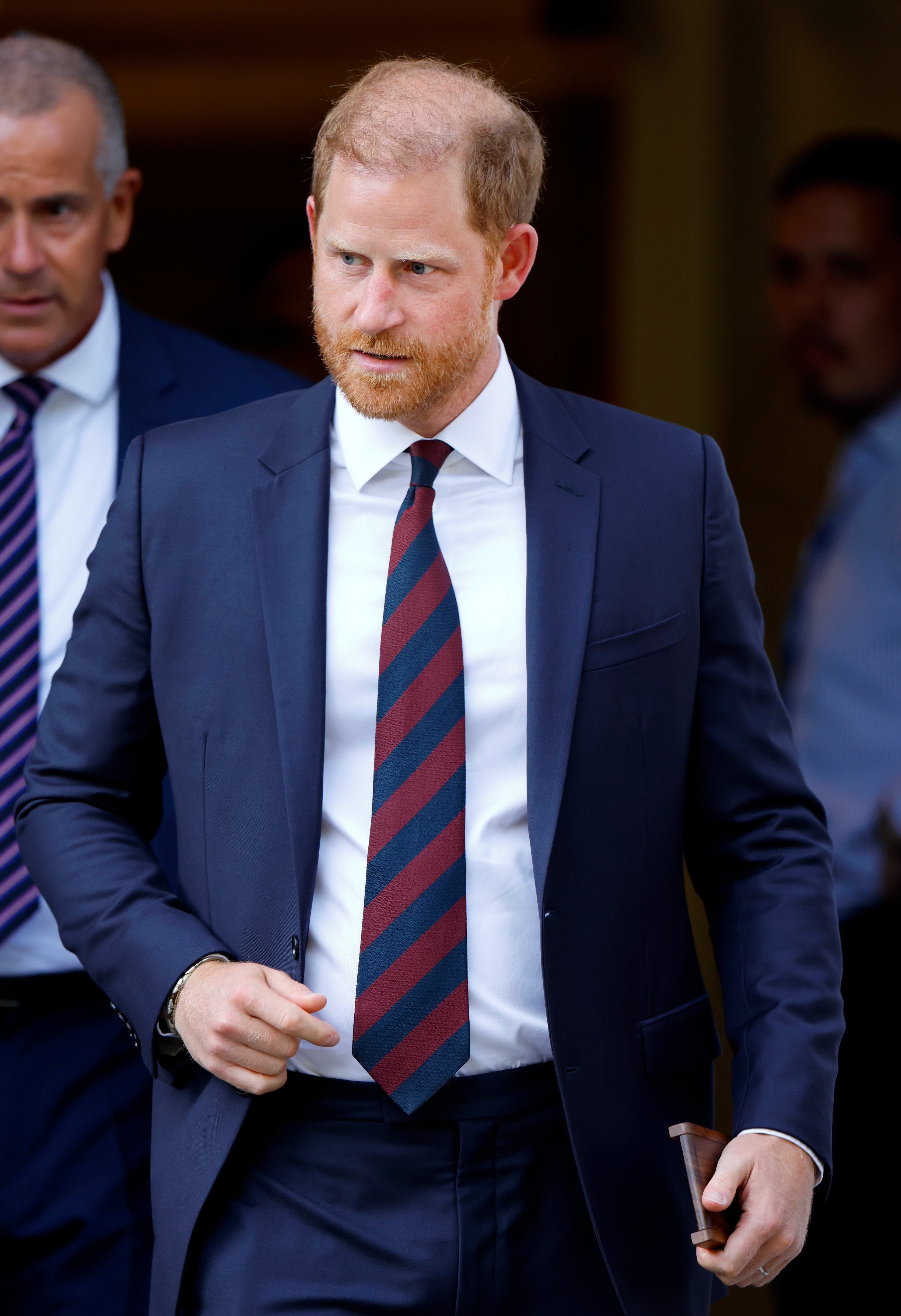 Prince Harry, Duke of Sussex, wearing a dark suit and striped tie, departs an Invictus Games Foundation event.