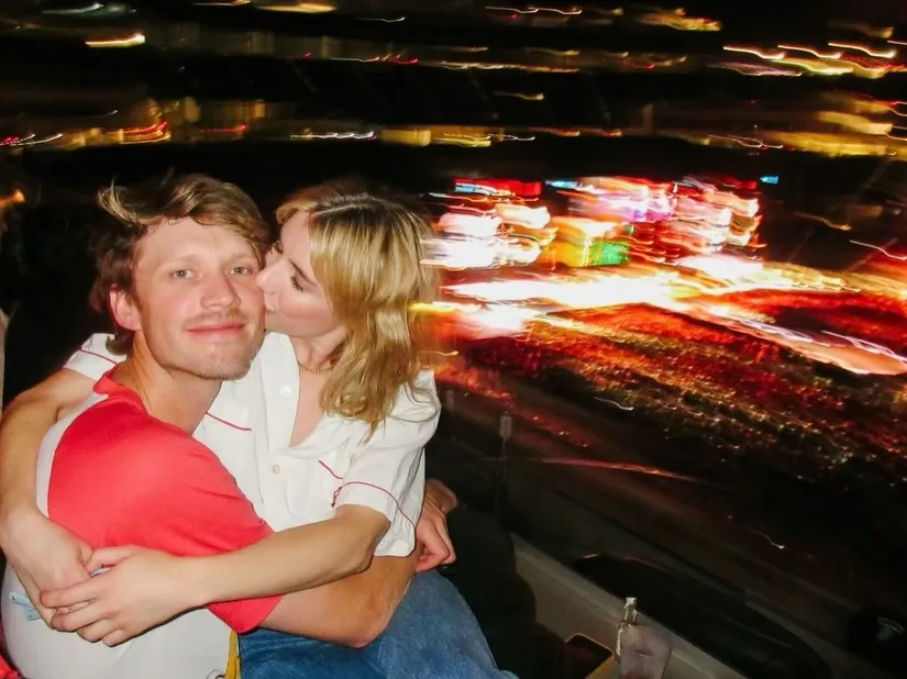 Emma Roberts and Cody John sitting and embracing each other at night with blurred lights in the background.