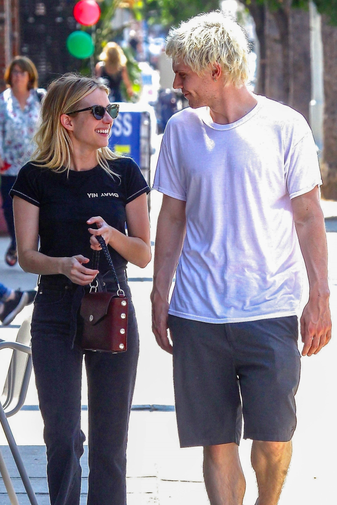 Emma Roberts and Evan Peters smiling at each other while walking outside.