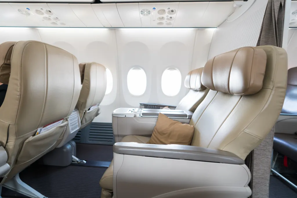 Empty beige leather airplane seats with small windows.