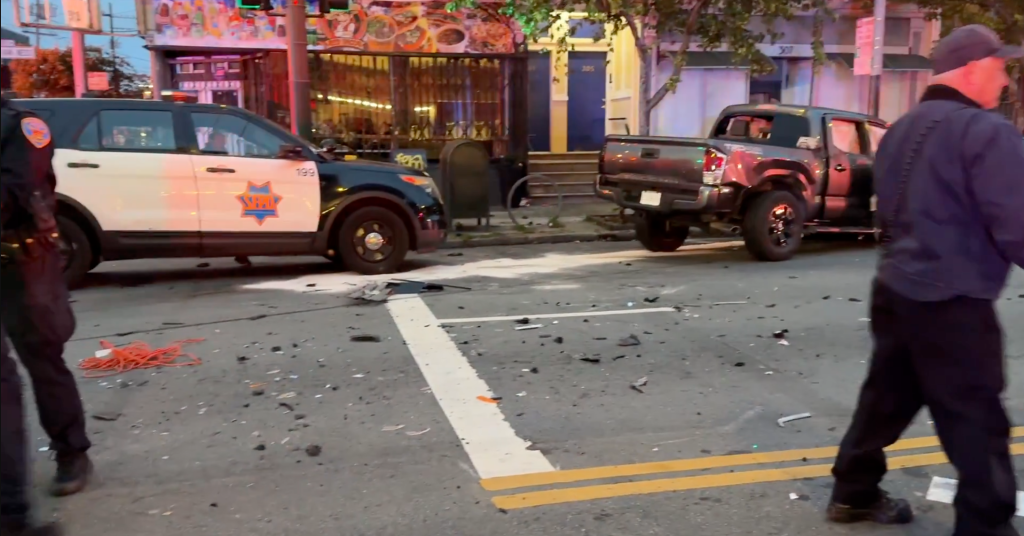 A San Francisco Police Department patrol car and a dark pickup truck involved in a multi-vehicle collision, with debris scattered on the street.