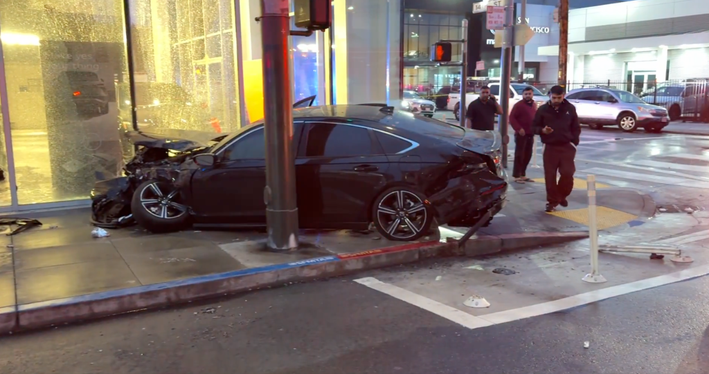 A dark sedan crashed into a light pole and building, with damage to the front and rear of the vehicle.