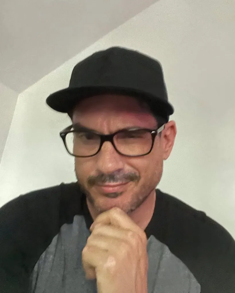 Ethan Browne wearing a black cap and glasses, with his hand on his chin.