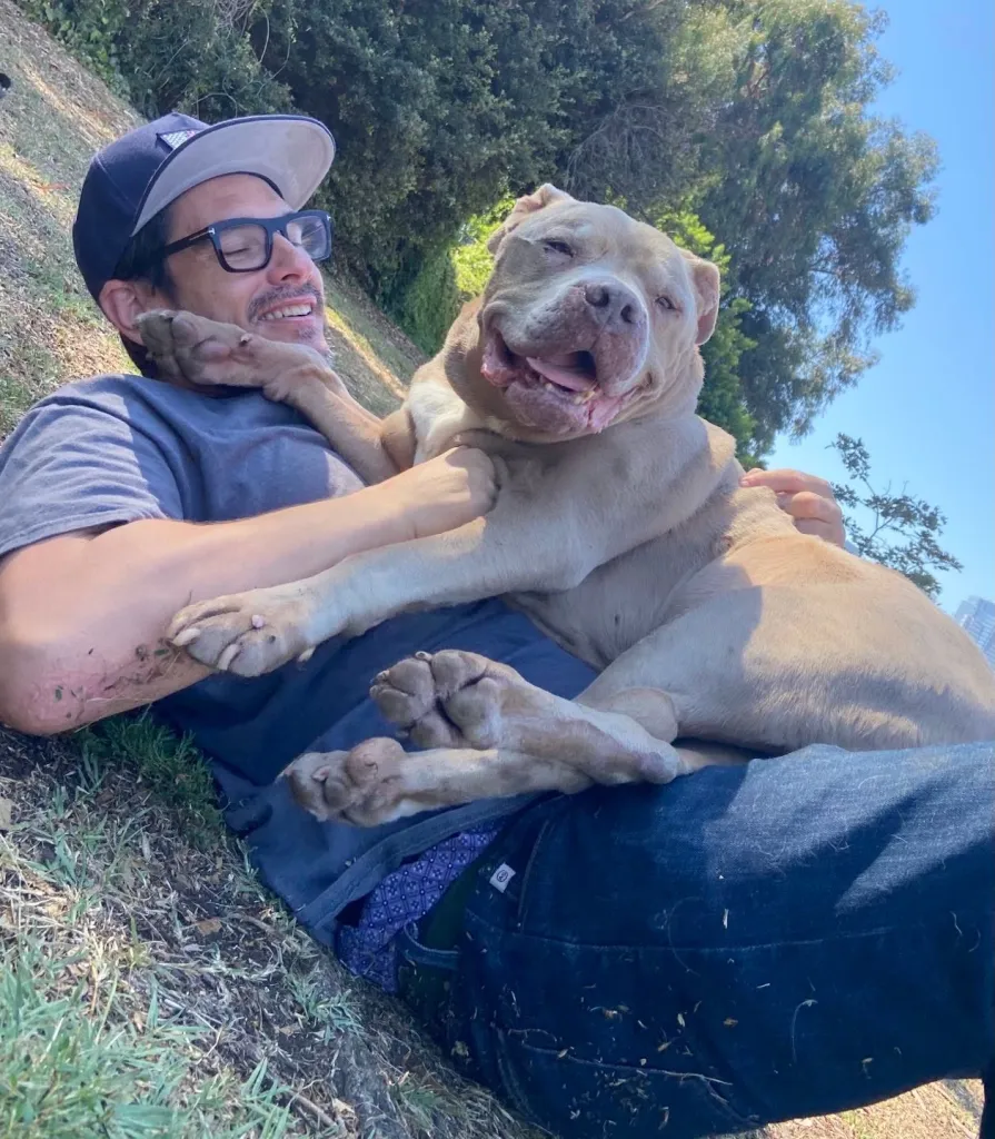 Ethan Browne lying on the grass with a tan dog lying on his chest and lap.