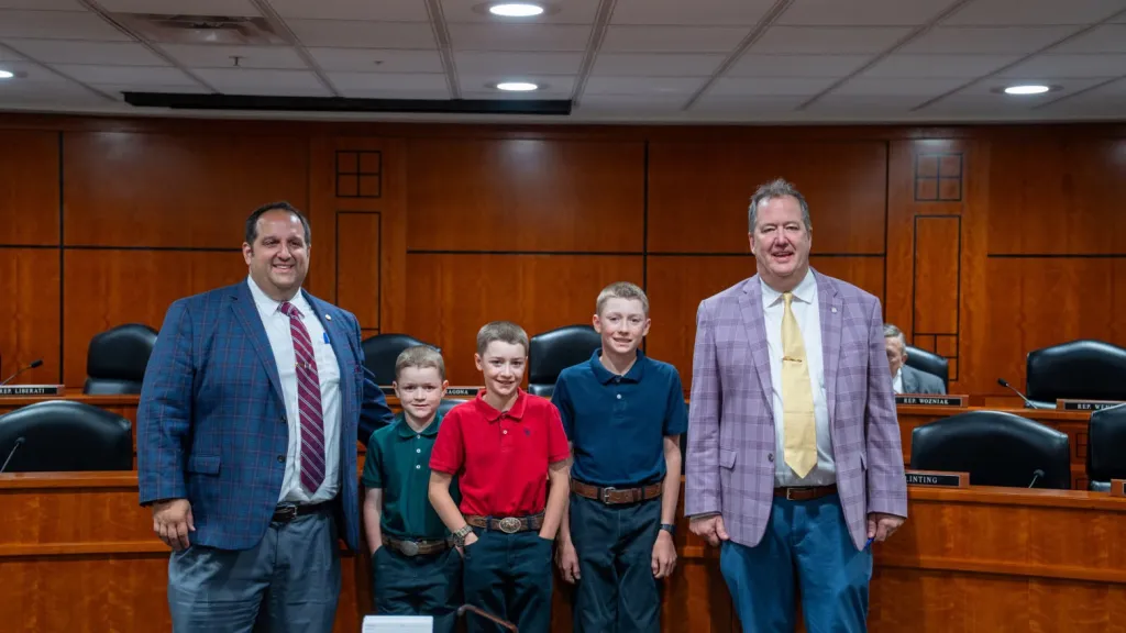 Ethan, Seth, and Jonathan Mielke with Rep. Cam Cavitt in a legislative chamber.