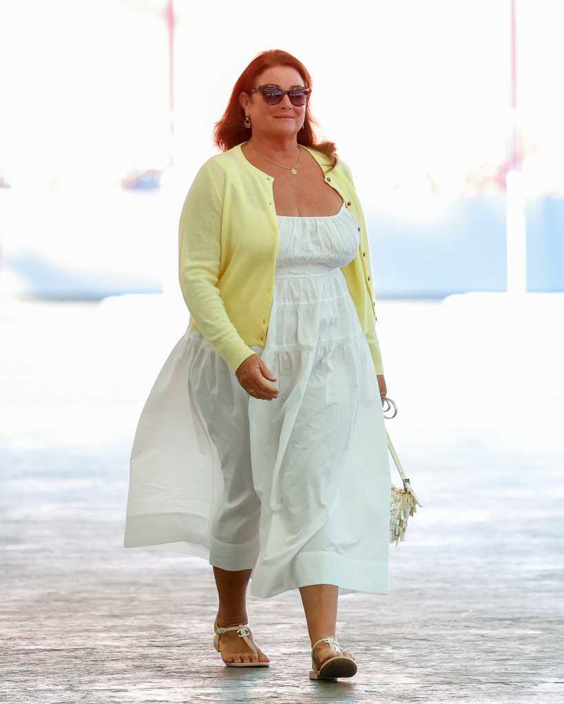Keely Shaye Smith walking while wearing a white dress, a yellow cardigan, and sunglasses.